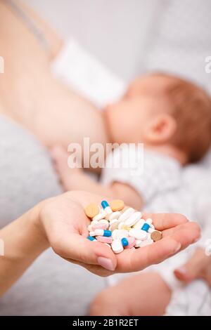 Mother holding handful of pills and tablets while breastfeeding newborn baby. Breastfeeding and medication concept Stock Photo