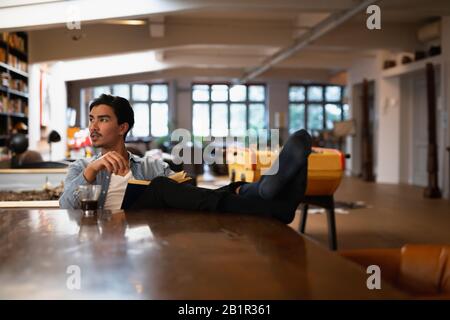 Young man reading a book with putting his feet on the table Stock Photo