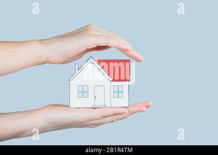 The figure of a house in human hands. Hands hold and gently cover a figure of home - concept of home insurance, safety, family planning, mortgage and Stock Photo
