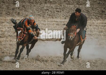 Tashkurgan, China - September 2019: Tajik horse-mounted men players pulling goat body during traditional Buzkashi game, riding fast running horses Stock Photo