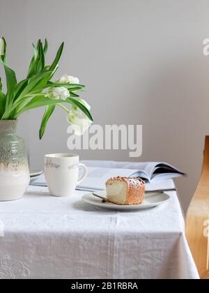 Table setting with a piece of cake and white tulips in vase Stock Photo