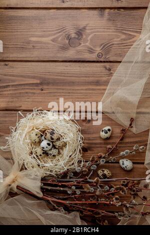 Easter quail eggs in nest and willow branch on a wooden background, copy space Stock Photo