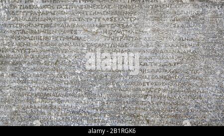 Ancient Greek writing on rock for background. Antique inscription carved on stone. Old script text close-up. Gray wall with historic letters. Vintage Stock Photo