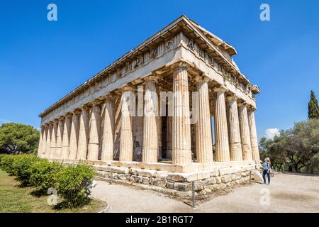 Temple of Hephaestus in summer, Athens, Greece. This ancient Greek building is one of the main landmarks of Athens. Young woman tourist looks at the f Stock Photo