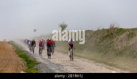 Viesly, France - April 14, 2019: The peloton riding on the dusty cobblestone road from Briastre to Viesly during Paris Roubaix 2019. Stock Photo