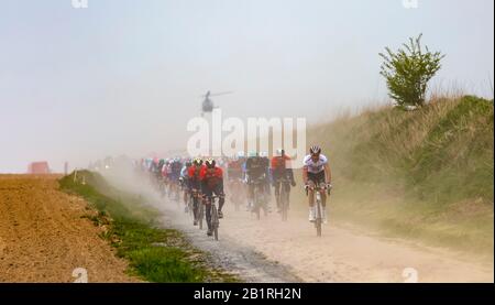 Viesly, France - April 14, 2019: The peloton riding on the dusty cobblestone road from Briastre to Viesly during Paris Roubaix 2019. Stock Photo