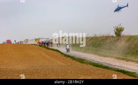 Viesly, France - April 14, 2019: The peloton riding on the dusty cobblestone road from Briastre to Viesly during Paris Roubaix 2019. Stock Photo