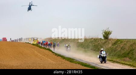 Viesly, France - April 14, 2019: The peloton riding on the dusty cobblestone road from Briastre to Viesly during Paris Roubaix 2019. Stock Photo