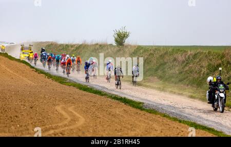 Viesly, France - April 14, 2019: The peloton riding on the dusty cobblestone road from Briastre to Viesly during Paris Roubaix 2019. Stock Photo