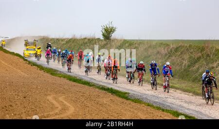 Viesly, France - April 14, 2019: The peloton riding on the dusty cobblestone road from Briastre to Viesly during Paris Roubaix 2019. Stock Photo