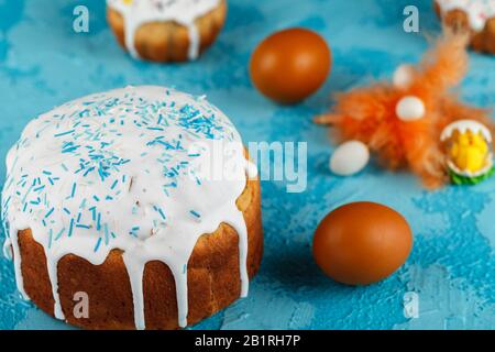 Fresh Easter cake, baked at home and decorated with sweet icing. Colored boiled eggs lie on the table as an element of the Easter holiday. Artificial Stock Photo
