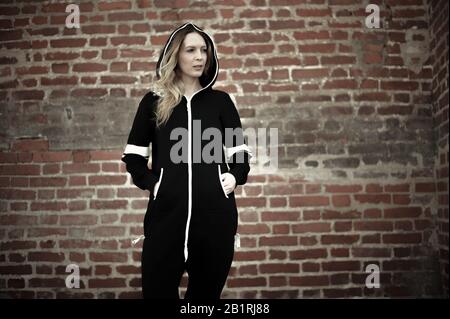 Street fashion. Young beautiful woman in fashionable cheeky modern black and white sports and casual overalls on a brick wall background Stock Photo