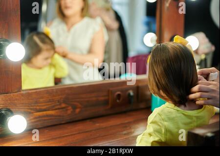 Baby girl comb her hair infront of mirror in dressing room with mom Stock Photo