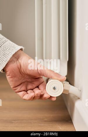 closeup of a caucasian man, wearing a pale gray sweater, rotating the valve of a hot-water radiator to increase or decrease its temperature Stock Photo