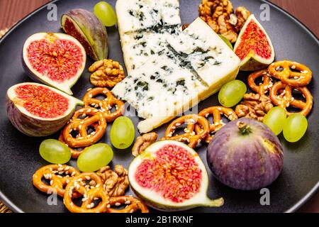 Cheese plate with blue cheese, honey, walnuts, figs, grapes, pretzels. Traditional healthy appetizer, snack, antipasti. Wooden boards background, vint Stock Photo