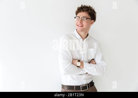 Handsome smiling confident young curly haired businessman wearing white shirt standing infront of isolated background, arms folded, laughing Stock Photo