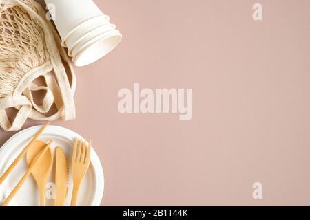 Zero waste, plastic free shopping concept. Mesh grocery bag, paper cups and plate, eco-friendly bamboo cutlery set on brown background. Sustainable li Stock Photo