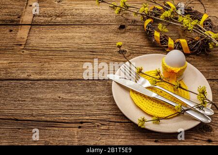 Easter table setting on old wooden background. Spring holiday card template. Cutlery, crochet napkin, egg, flowering sprigs of dogwood, birch wreath, Stock Photo