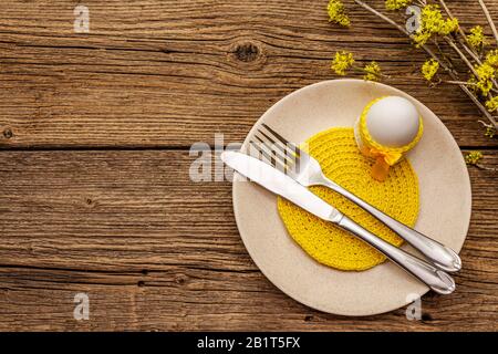 Easter table setting on old wooden background. Spring holiday card template. Cutlery, crochet napkin, egg, flowering sprigs of dogwood, top view Stock Photo