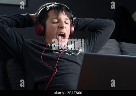 Tired teenage boy , 13,  yawns as he watches online videos on laptop Stock Photo