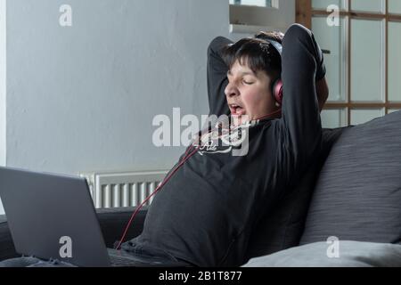 Tired teenage boy , 13,  yanws as he watches online videos on laptop Stock Photo