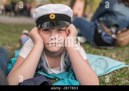 Portrait of a young girl with a traditional student hat lying on the ground at the Valborg celebration in Uppsala, Sweden Stock Photo