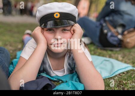 Portrait of a young girl with a traditional student hat lying on the ground at the Valborg celebration in Uppsala, Sweden Stock Photo