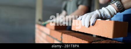 Two workers making red brick wall at construction site Stock Photo