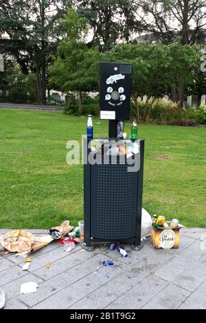 Full litter bin overflowing with rubbish in a public park after a party. France Stock Photo