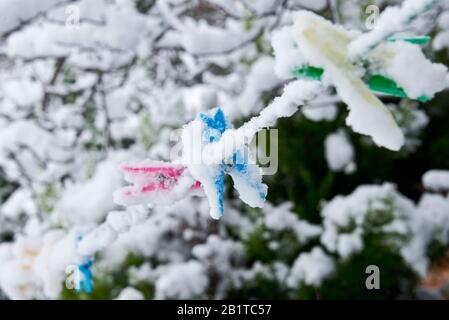 Brightly coloured plastic pegs hanging from a washing line covered in snow in a back garden with snow covered trees in the background in Taunton Stock Photo