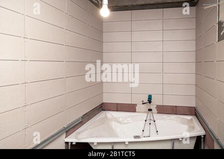 Bathroom interior with rectangular ceramic tiles on walls, electronic level in bath, repair, reconstruction, even rows of new tile Stock Photo
