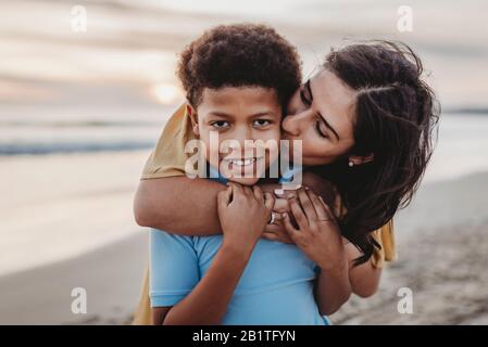 Close up of mother kissing school-aged boy at beach during sunset