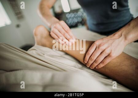 Massage therapist uses her hands to work on calf of patient Stock Photo