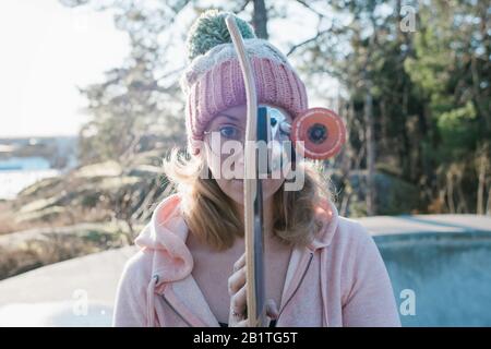 portrait of a woman holding her skateboard in front of her face Stock Photo