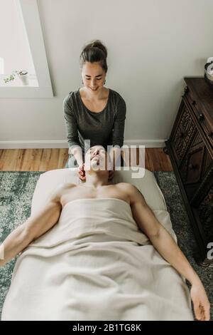 smiling female massage therapist treats neck of male patient Stock Photo