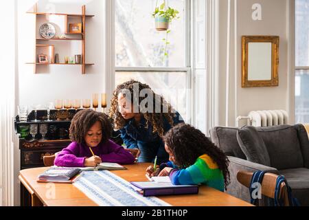 Mother assisting daughter in doing homework at table in living room Stock Photo