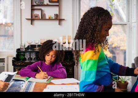 Girl doing homework while sister standing by table in living room Stock Photo