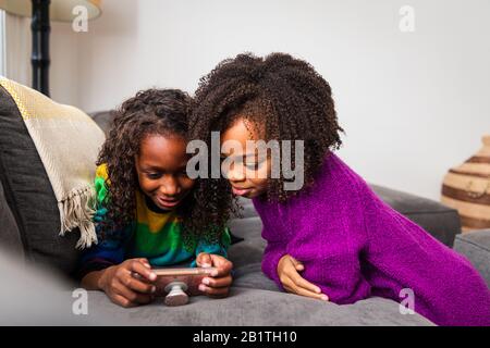 Girl looking at sister using mobile phone on sofa at home Stock Photo