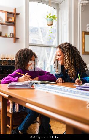 Smiling daughter looking at mother while studying at home Stock Photo