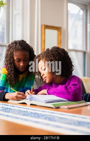 Girl assisting sister in doing homework at table Stock Photo