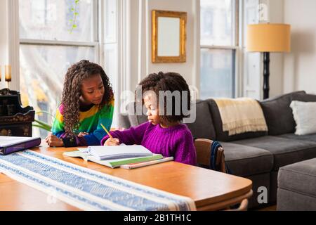 Girl assisting sister in doing homework at table in living room Stock Photo