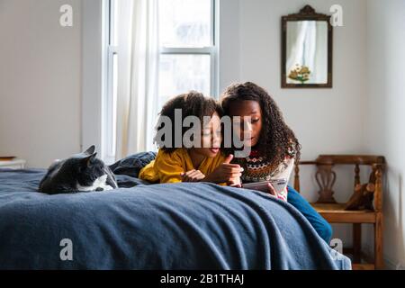 Girl showing smart phone to sister while lying by cat on bed at home Stock Photo