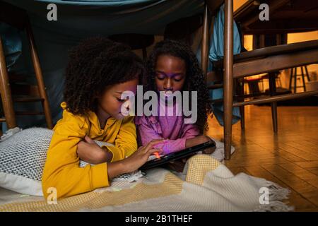 Sisters using digital tablet while lying on blanket at home Stock Photo