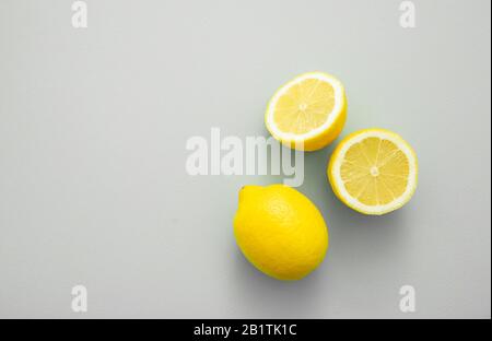 Ripe juicy lemons on gray background. Whole yellow lemon and lemon cut half, top view, copy space. Fresh citrus fruits, vitamin c source Stock Photo