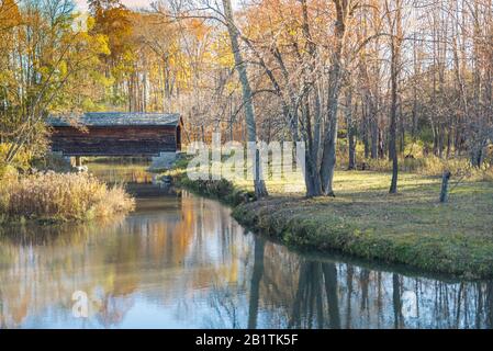 Covered bridge in the autumn with reflections in a creek Stock Photo