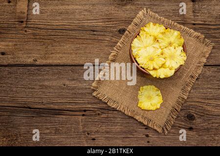 Dried slices of pineapple in bowl. Fruit snack, healthy eating concept. Sackcloth, old wooden boards background, top view, copy space Stock Photo