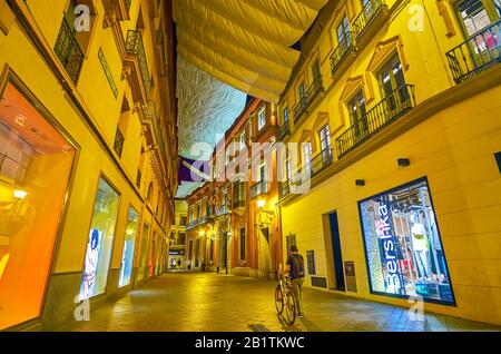 SEVILLE, SPAIN - OCTOBER 1, 2019: The bright illuminated historical houses with awnings in shopping area of central district, on October 1 in Seville Stock Photo