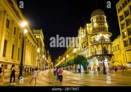 SEVILLE, SPAIN - OCTOBER 1, 2019: The crowds of tourists walk in Seville, making pictures of amazing night illuminated buildings or just exploring nig Stock Photo