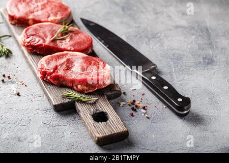 Three pieces of traditional thin steak cut from the tenderloin on wooden cutting board with olive oil, salt, rosemary and pepper. Raw Black Angus Prim Stock Photo