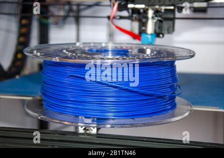 View of coil of blue plastic for 3D printing on printer background. Plastic for 3D printing. Blue plastic filament, ABS/PLA coil Stock Photo